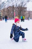 adorable niña sentada en el hielo con patines después de la caída foto