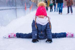 Little adorable girl sitting on ice with skates after fall photo