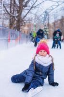 Little adorable girl sitting on ice with skates after fall photo