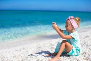 Little cute girl taking pictures on phone at tropical beach photo