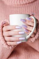 manos de niña con delicada manicura púrpura sosteniendo una taza de té. foto