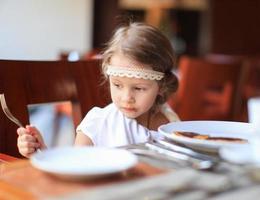 Adorable little girl having breakfast at restaurant photo