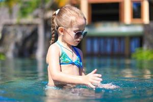 Little cute happy girl in swimming pool during summer vacation photo