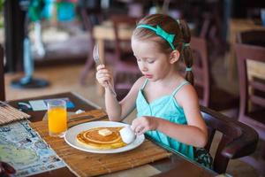 Adorable little girl having breakfast at resort restaurant photo