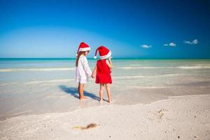 Little adorable girls in Santa hats during beach vacation photo