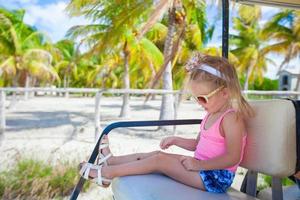 Little adorable girl in golf car at palm grove during tropical vacation photo
