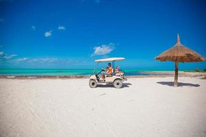 Dad and his little girls driving golf cart on tropical beach photo