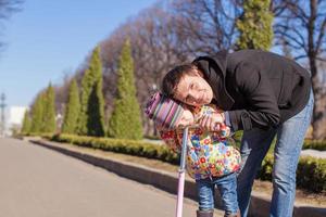 Adorable little girl and happy father ride on scooter outdoors photo