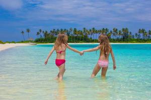 Adorable happy little girls have fun at shallow water on beach vacation photo