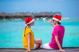 pareja joven con sombreros de santa relajándose en un embarcadero de madera en vacaciones de navidad foto