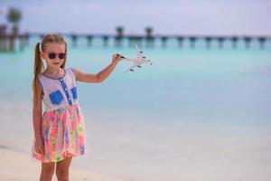 niña feliz con avión de juguete en las manos en la playa de arena blanca foto