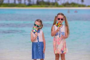 Two little girls with bright tasty lollipops on white beach photo