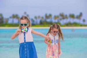 Two little girls with bright tasty lollipops on white beach photo