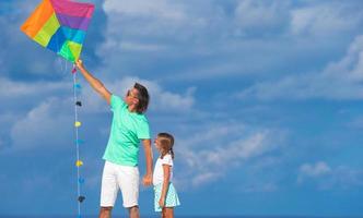 Happy father and little girl flying kite together at tropical beach photo