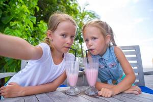 Little girls taking selfie and drinking tasty cocktails at outdoor cafe photo
