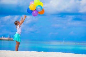 Adorable little girl playing with colorful balloons at tropical beach photo