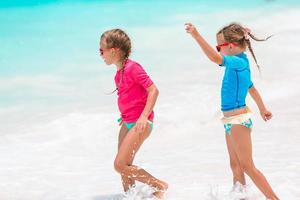 Little happy funny girls have a lot of fun at tropical beach playing together. Sunny day with rain in the sea photo