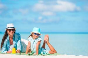 la madre pone crema de protección solar en la pequeña hija en la playa en un caluroso día de verano foto