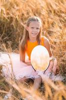 Adorable preschooler girl walking happily in wheat field on warm and sunny summer day photo