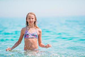 Happy child splashing in the waves during summer vacation on tropical beach. Girl play at the sea. photo