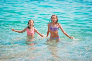 niños felices chapoteando en las olas durante las vacaciones de verano en la playa tropical. las niñas juegan en el mar. foto