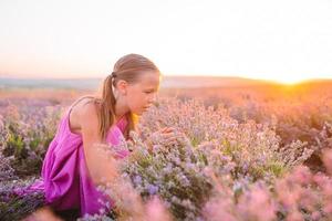 Cute girl in lavender flowers field at sunset in purple dress photo