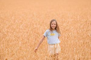 Adorable preschooler girl walking happily in wheat field on warm and sunny summer day photo