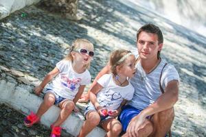 Young father with little daughters sitting on street in old greek town photo