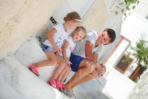 Happy father and cute daughters sitting on street in old greek town photo