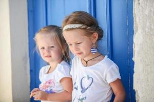 retrato de niñas sonrientes sentadas cerca de la antigua puerta azul en el pueblo griego, emporio, santorini foto