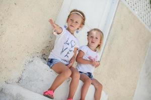 Little cute sisters sitting near old house in Greek village of Emporio, Santorini photo