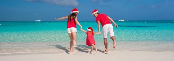 Happy family of three in Christmas Hats having fun on white beach photo