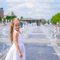 una niña feliz se divierte en la fuente de la calle en un día caluroso y soleado foto