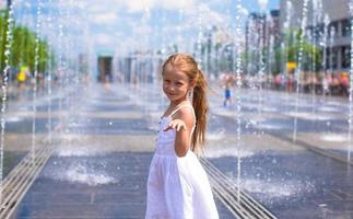 una niña feliz se divierte en la fuente de la calle en un día caluroso y soleado foto