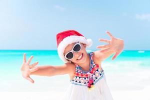 adorable niña con sombrero de santa durante las vacaciones navideñas en la playa foto