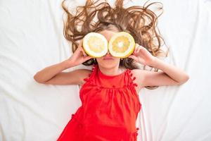 Little girl covering eyes with lemon halves near eyes photo
