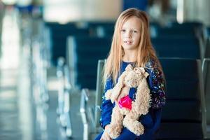 niña adorable en el aeropuerto cerca de una gran ventana con su juguete favorito listo para viajar foto