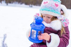 Little cute girl warms her hands on candle in blue lantern in winter time photo