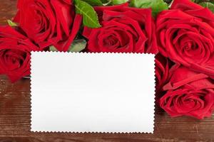 Red roses bouquet and white paper sheet for text on old rustic wooden table close up. Copy space. photo