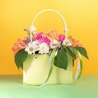 Beautiful flowers bouquet in gift light green paper bag with ribbons on yellow-green background. photo