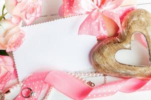 Pink roses, gift box, wooden heart, pink ribbon, jewelry, blank sheet close up. Jewelry shop sale. photo