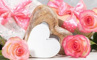 Gift boxes with pink polka dots bows, gentle peach color roses, empty white wooden heart. Close up. photo