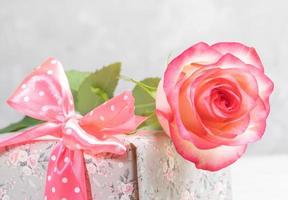 Pale pink rose on gift box wrapped in floral paper and decorated pink polka dots bow close up. photo