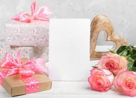 Festive composition with gift boxes, peach color roses, wooden heart, empty white blank for text. photo