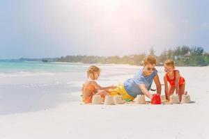 padre e hijos haciendo castillos de arena en la playa tropical. familia jugando con juguetes de playa foto