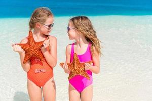 Adorable little girls with starfish on white beach photo