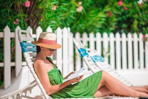 Young woman reading book on chaise-lounge on the beach photo