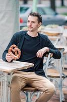 hermoso joven sosteniendo pretzel y relajándose en el parque foto