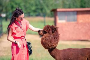 Happy woman is playing with cute alpaca in the park photo