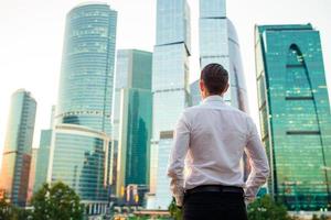 Back view of businessman looking on copy space while standing against glass skyscraper photo